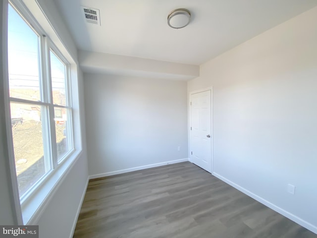 empty room featuring dark wood-style floors, visible vents, and baseboards