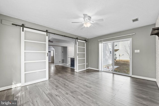 unfurnished living room featuring visible vents, a barn door, ceiling fan, wood finished floors, and baseboards