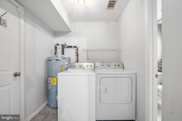 washroom featuring laundry area, visible vents, washer and clothes dryer, electric water heater, and light tile patterned flooring