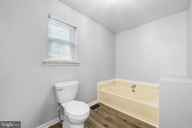 full bath featuring a garden tub, toilet, a textured ceiling, wood finished floors, and baseboards