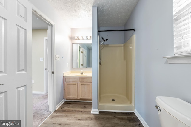 full bath featuring a stall shower, baseboards, wood finished floors, a textured ceiling, and vanity