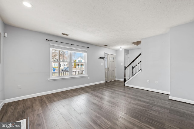 unfurnished living room featuring a textured ceiling, visible vents, baseboards, stairway, and dark wood-style floors