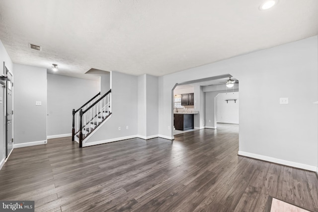 unfurnished living room featuring dark wood-type flooring, visible vents, baseboards, and stairs