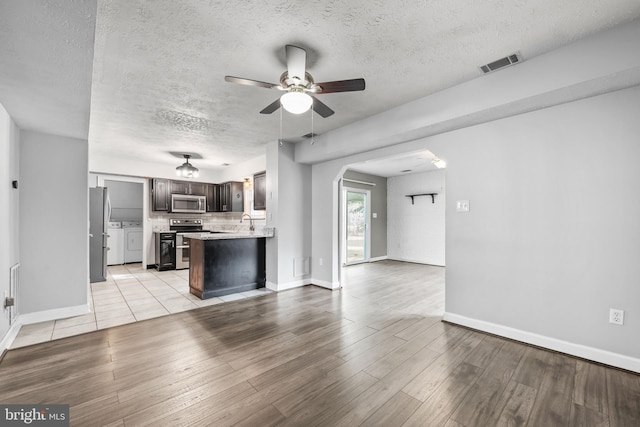 unfurnished living room featuring arched walkways, visible vents, washer and clothes dryer, light wood-style floors, and a sink