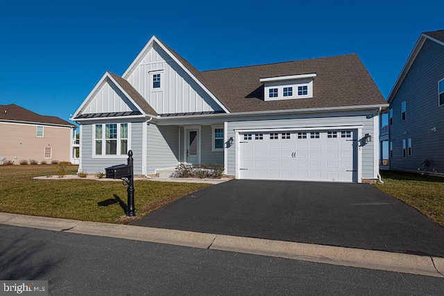 view of front facade with board and batten siding, a front yard, a standing seam roof, an attached garage, and aphalt driveway