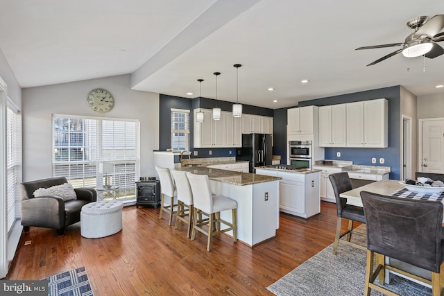 kitchen featuring stainless steel double oven, white cabinets, a center island, black refrigerator with ice dispenser, and decorative light fixtures