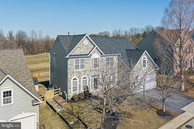 traditional home featuring driveway, stone siding, and roof with shingles