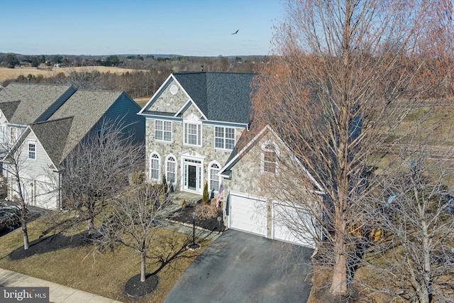 traditional-style home featuring driveway, stone siding, a shingled roof, and a garage