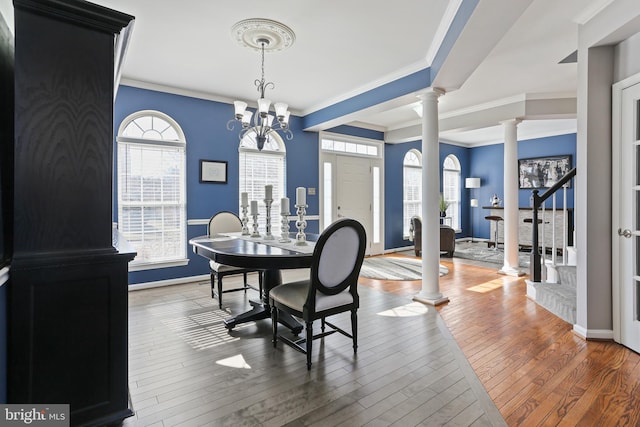 dining space featuring baseboards, wood finished floors, stairs, crown molding, and ornate columns