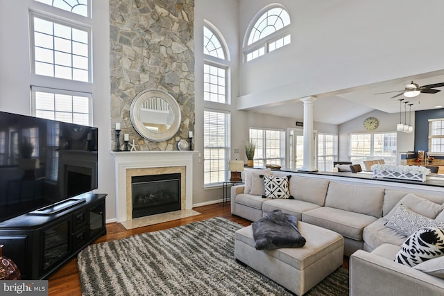 living area featuring a fireplace, a towering ceiling, dark wood-type flooring, ceiling fan, and ornate columns