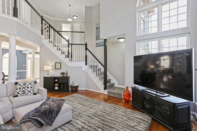 living room with decorative columns, baseboards, a towering ceiling, dark wood-type flooring, and stairs