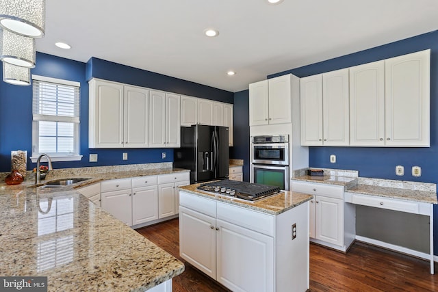 kitchen featuring white cabinets, light stone counters, appliances with stainless steel finishes, a center island, and a sink