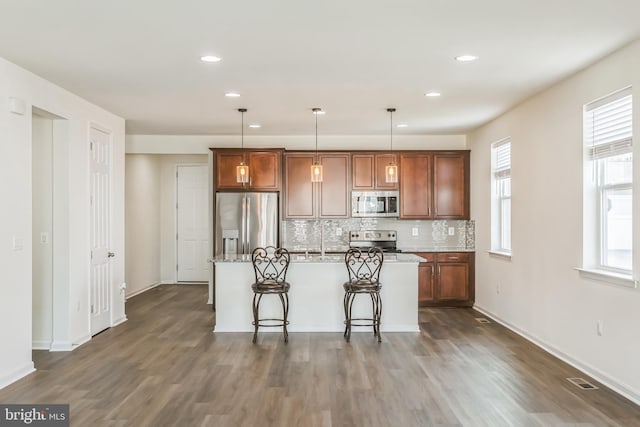 kitchen with an island with sink, appliances with stainless steel finishes, hanging light fixtures, and a breakfast bar