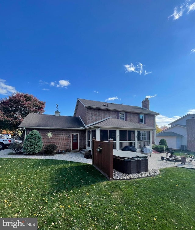 rear view of property featuring a yard, a chimney, a hot tub, a patio area, and brick siding