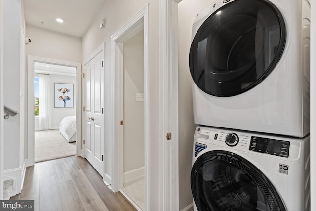 laundry area featuring stacked washer and dryer and light hardwood / wood-style flooring