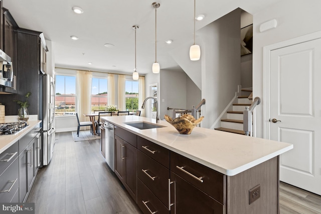 kitchen with a center island with sink, appliances with stainless steel finishes, hanging light fixtures, dark brown cabinetry, and sink