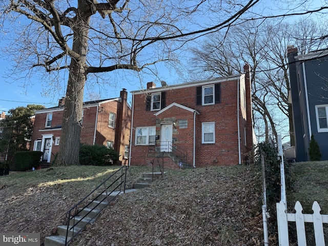 view of front facade featuring brick siding, a chimney, and fence