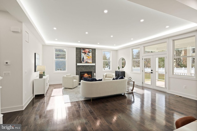 living area with a tray ceiling, dark wood finished floors, a wealth of natural light, and a glass covered fireplace