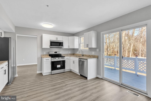 kitchen featuring appliances with stainless steel finishes, white cabinetry, visible vents, and light wood finished floors