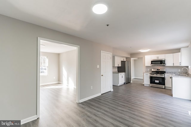 kitchen with stainless steel appliances, light countertops, white cabinets, a sink, and wood finished floors