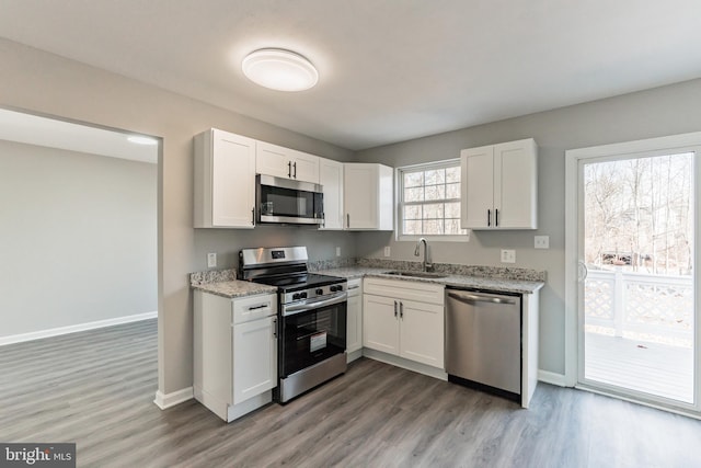 kitchen with stainless steel appliances, a sink, white cabinetry, and light stone countertops