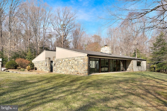 exterior space featuring stone siding, a lawn, and a chimney