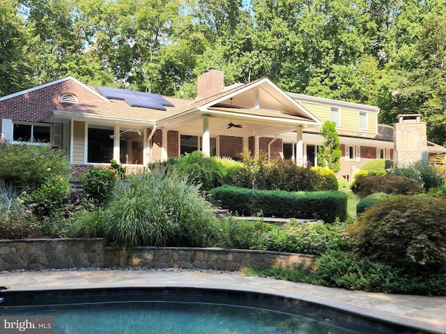 view of front facade with brick siding, a chimney, solar panels, a ceiling fan, and an outdoor pool