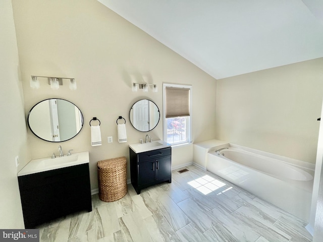 bathroom with lofted ceiling, two vanities, a garden tub, and a sink