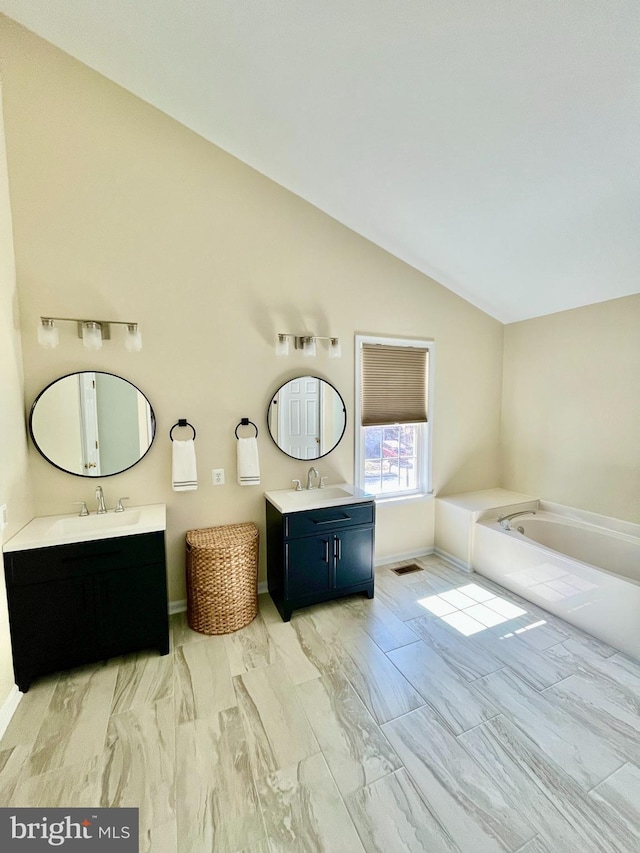 full bathroom featuring a sink, two vanities, a garden tub, and vaulted ceiling