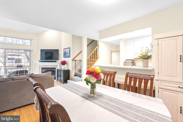 dining area featuring stairs, a glass covered fireplace, and light wood-type flooring