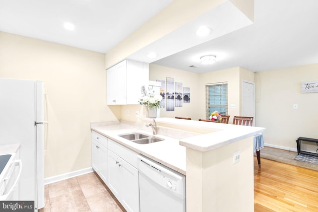 kitchen featuring a peninsula, white appliances, light countertops, and a sink