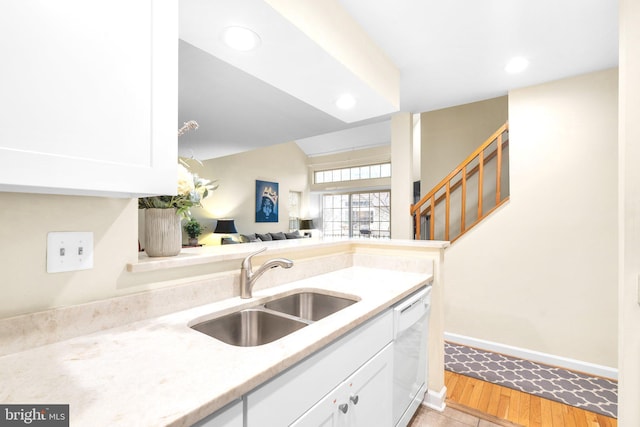 kitchen with baseboards, open floor plan, white dishwasher, white cabinetry, and a sink