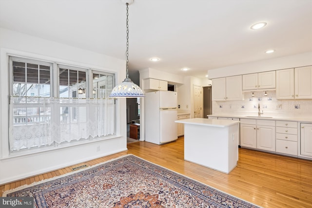 kitchen with light wood-style floors, freestanding refrigerator, white cabinetry, and a sink