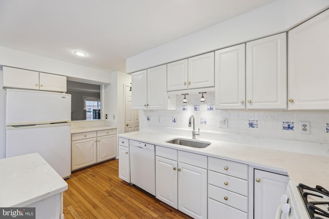 kitchen with light wood-style flooring, white appliances, a sink, white cabinets, and tasteful backsplash