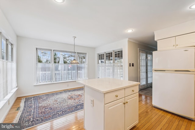 kitchen with light countertops, light wood-style flooring, hanging light fixtures, and freestanding refrigerator