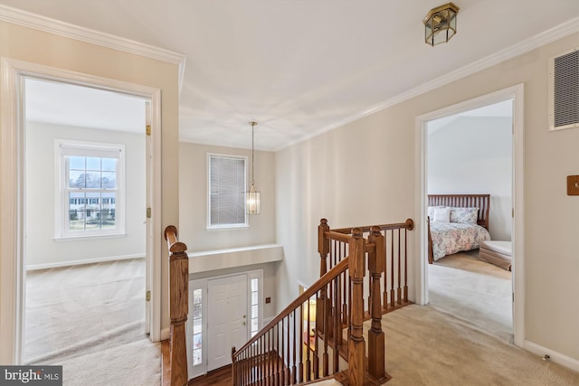 hall with carpet floors, ornamental molding, and an upstairs landing