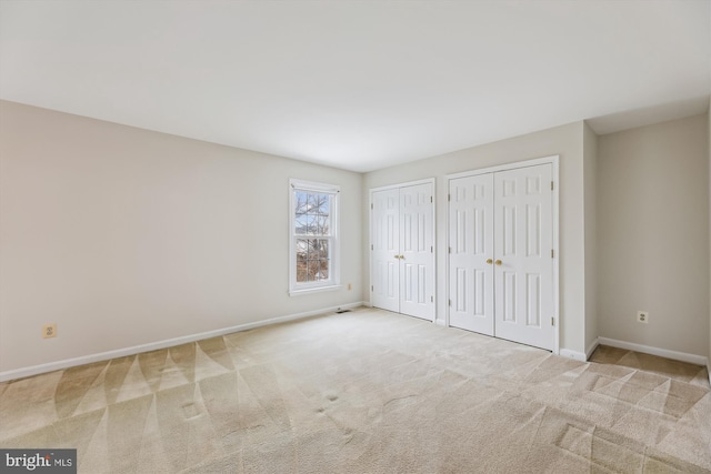 unfurnished bedroom featuring multiple closets, carpet, and baseboards