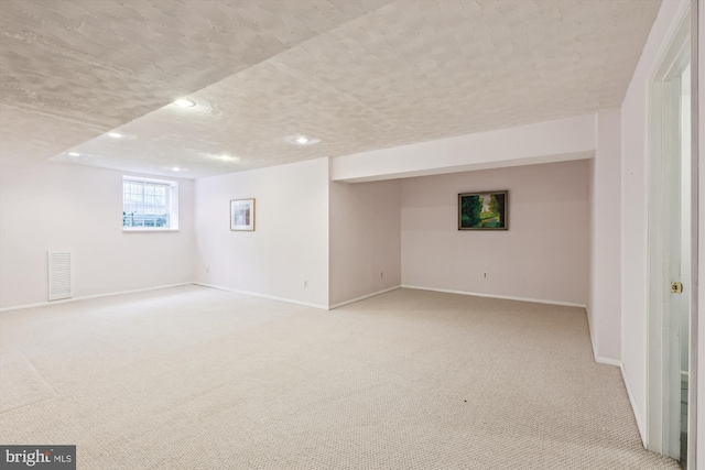 below grade area featuring baseboards, a textured ceiling, visible vents, and light colored carpet