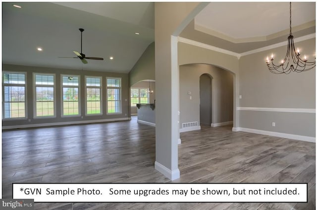 interior space with a towering ceiling, dark hardwood / wood-style flooring, a raised ceiling, crown molding, and ceiling fan with notable chandelier