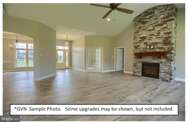 unfurnished living room featuring light hardwood / wood-style flooring, ceiling fan with notable chandelier, french doors, high vaulted ceiling, and a fireplace