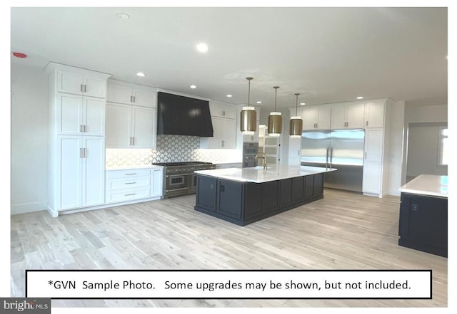 kitchen featuring high quality appliances, hanging light fixtures, exhaust hood, an island with sink, and white cabinets