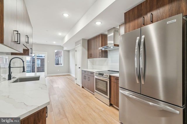 kitchen with light wood-style flooring, appliances with stainless steel finishes, a sink, wall chimney range hood, and modern cabinets