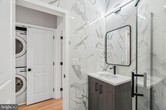 full bathroom with wood finished floors, vanity, tile walls, a shower stall, and stacked washer and clothes dryer