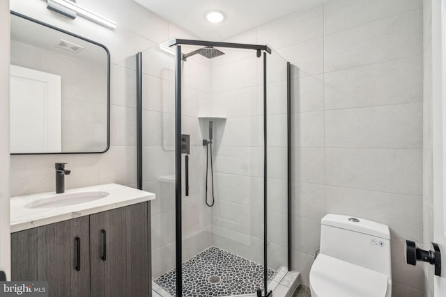 bathroom with toilet, a shower stall, tile walls, and vanity