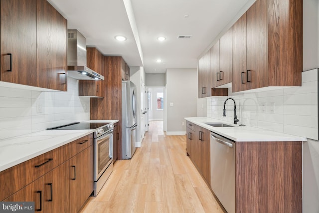 kitchen featuring a sink, wall chimney range hood, appliances with stainless steel finishes, light wood finished floors, and modern cabinets