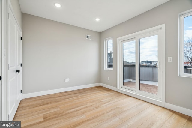 unfurnished room with a wealth of natural light, light wood-type flooring, visible vents, and baseboards