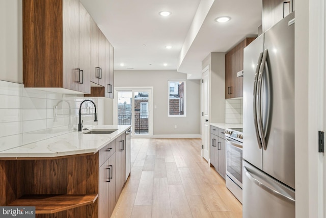 kitchen featuring light wood finished floors, modern cabinets, appliances with stainless steel finishes, light stone countertops, and a sink