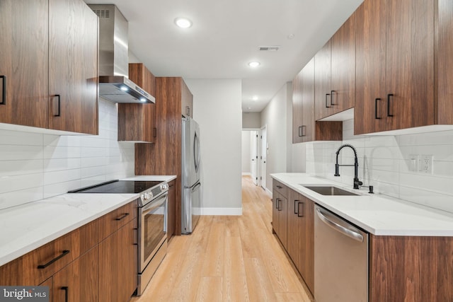 kitchen featuring stainless steel appliances, a sink, wall chimney range hood, light wood-type flooring, and modern cabinets