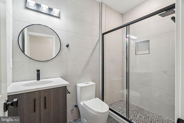 bathroom featuring a stall shower, tile walls, vanity, and toilet