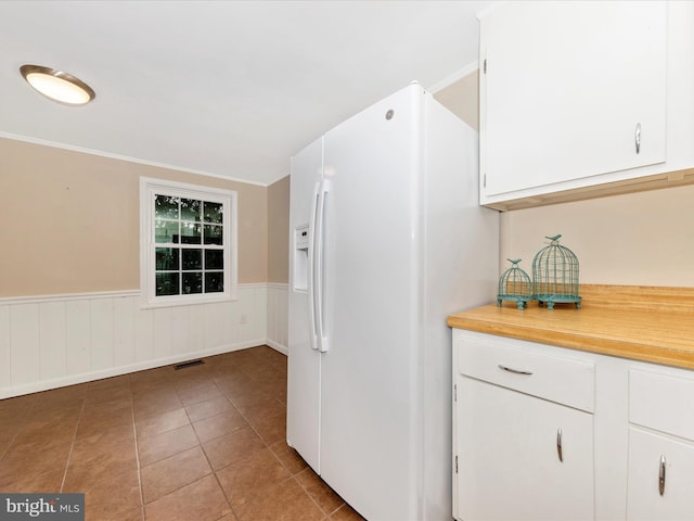 kitchen with white cabinetry, white fridge with ice dispenser, dark tile patterned floors, and ornamental molding